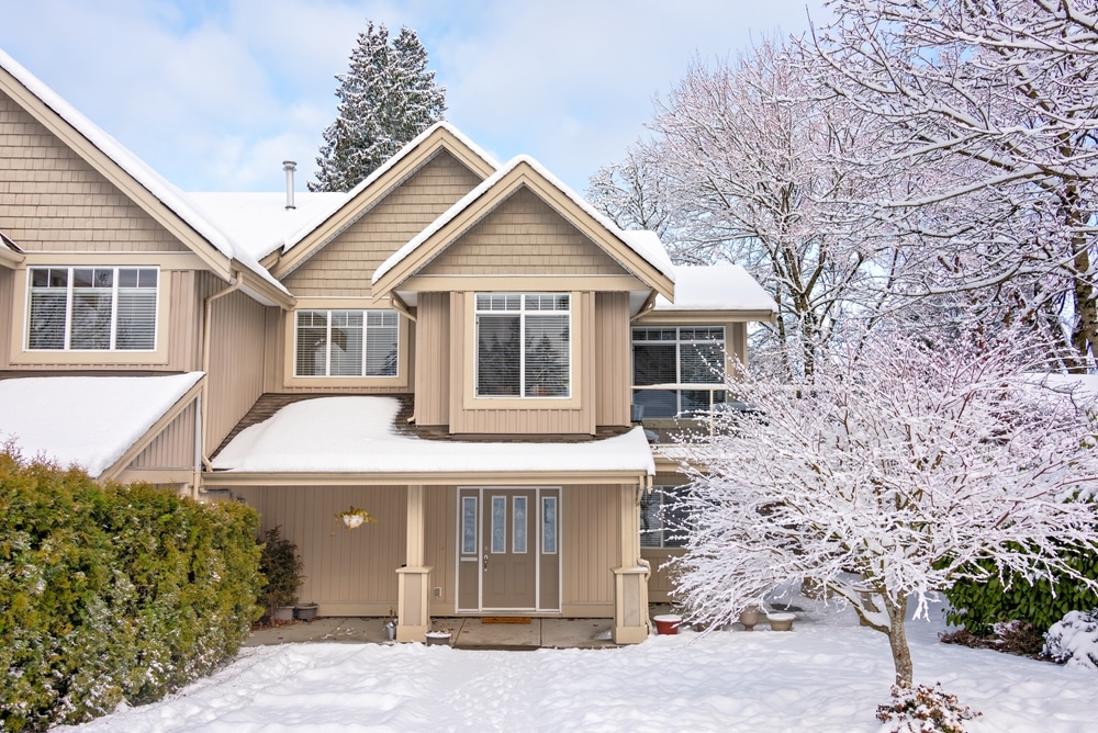 beige house in winter with snow covered yard and tree